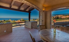 A terrace with a table and chairs, a bottle of wine, and a view of the sea and rocky landscape. - Villa La Dimora del Falco (Trinità d'Agultu e Vignola)