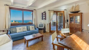 Ein Wohnzimmer mit Meerblick, einem Holzespeisetisch, einem blauen Sofa und einem Schrank mit einem Schiffmodell.