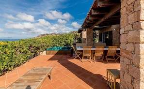 A patio with a stone table and chairs, a wooden deck, and a stone wall.