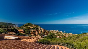 Un villaggio costiero con edifici a tetti in terracotta, un cielo azzurro limpido e vista sul mare.