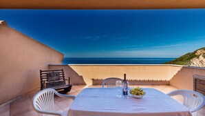 Un tavolo apparecchiato per due con vista sul mare, una bottiglia di vino e una ciotola di uva su una terrazza.