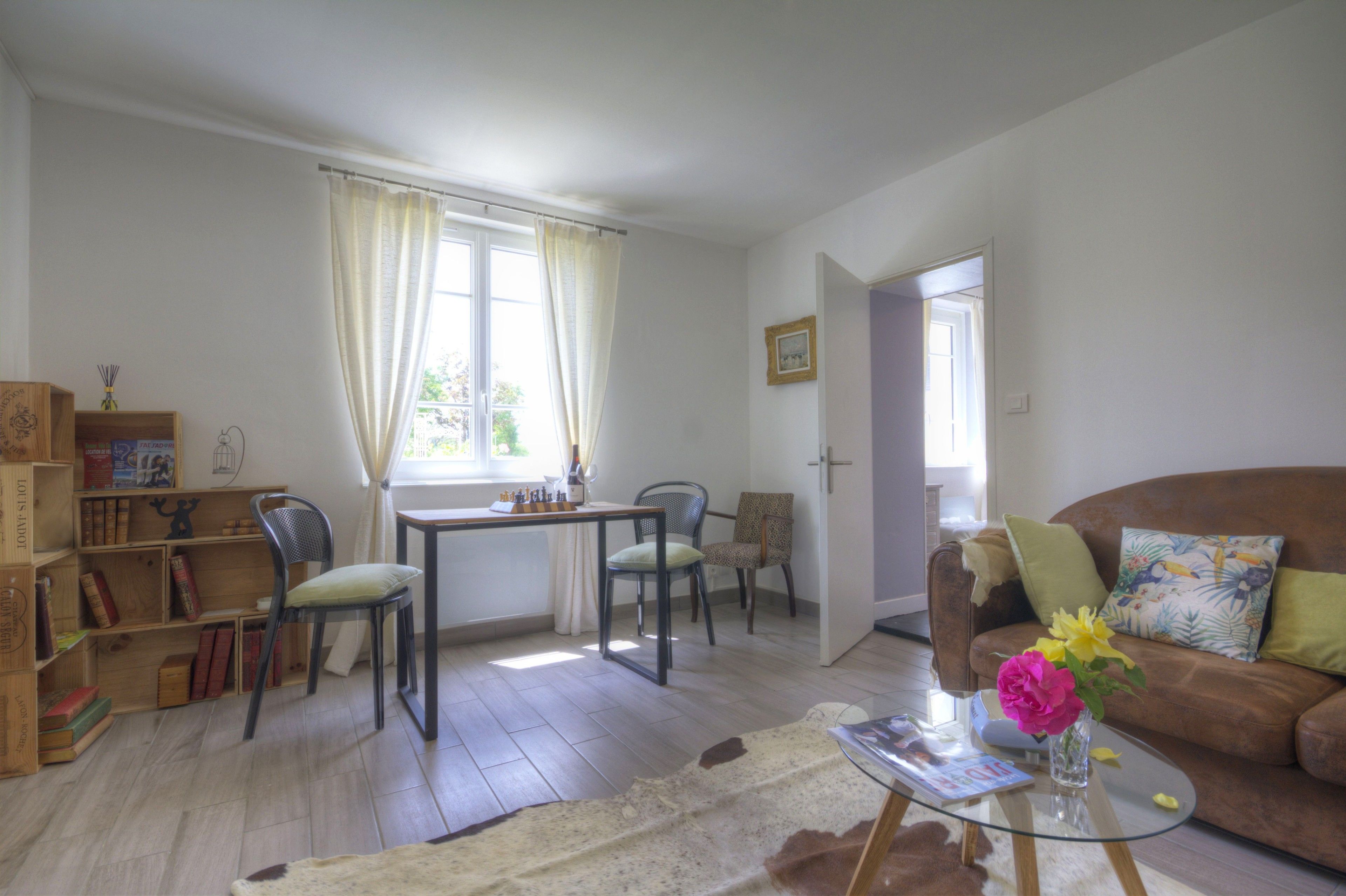 Una sala de estar con un sofá, una mesa de centro con un jarrón, una mesa de comedor con sillas y una estantería.