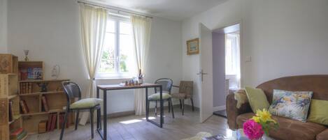 Una sala de estar con un sofá, una mesa de centro con un jarrón, una mesa de comedor con sillas y una estantería.