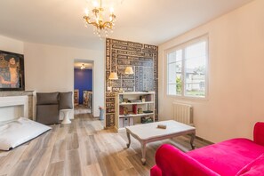 A room with a wooden floor, a red sofa, a white table, a bookshelf, and a chandelier. - L'Escale de Jules et Lily (Bligny-lès-Beaune)