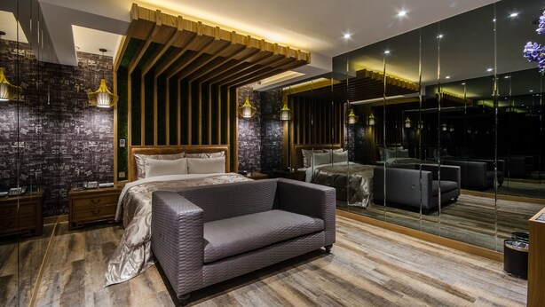 A modern bedroom with a large bed, a sofa, a mirror, and a cityscape wallpaper. - HE&LE Design Hotel (Taichung)