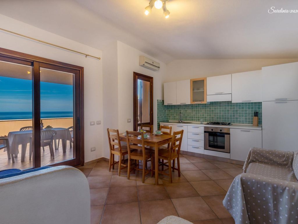 A compact kitchen with white cabinets, a green tiled backsplash, and a dining area with a table and chairs.