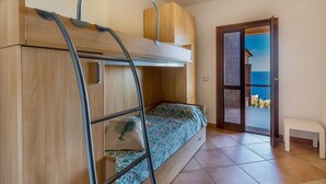 A room with a bunk bed, a ladder, a bench, and a door leading to a balcony with a view. - Casa Rosa Quattro (Trinità d'Agultu e Vignola)
