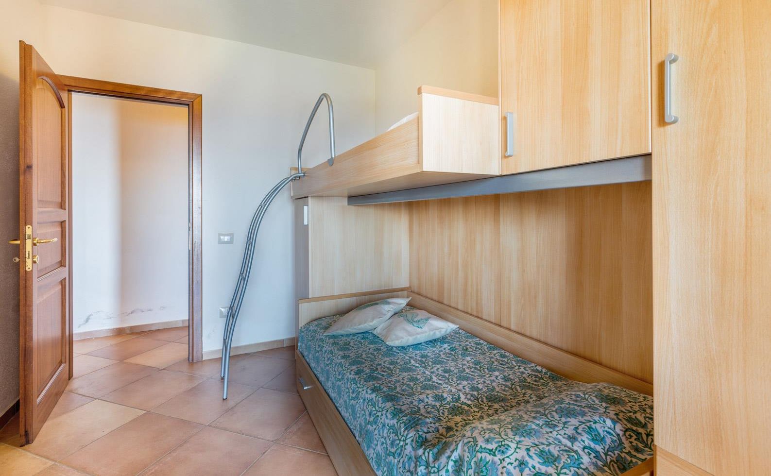 Una stanza piccola con un letto a castello, una porta in legno e un mobiletto.