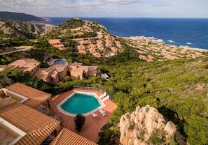 A coastal resort with terraced buildings, a swimming pool, and a view of the sea.