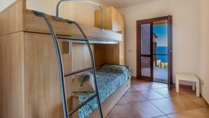 A compact bedroom with a bunk bed, a small bedside table, and a view of the sea through an open door. - Casa Rosa Due (Trinità d'Agultu e Vignola)