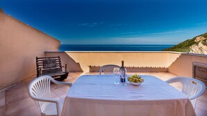 A table set with a bottle, glasses, and a bowl of grapes on a terrace with a view of the sea. - Casa Rosa Due (Trinità d'Agultu e Vignola)