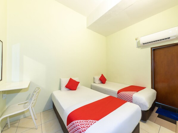 A hotel room with two single beds, a small desk, a chair, and an air conditioning unit.