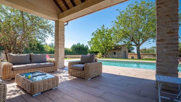 Une terrasse extérieure avec des meubles en osier, une piscine et un mur en pierre.