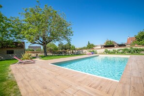 Ein rechteckiger Swimmingpool mit Holzterrasse, umgeben von einer Steinmauer und Grünpflanzen.