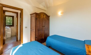 A bedroom with two single beds, a wooden wardrobe, a washing machine in the adjacent room, and a window with natural light. - Villa Violetta 1 Bianca (Trinità d'Agultu e Vignola)