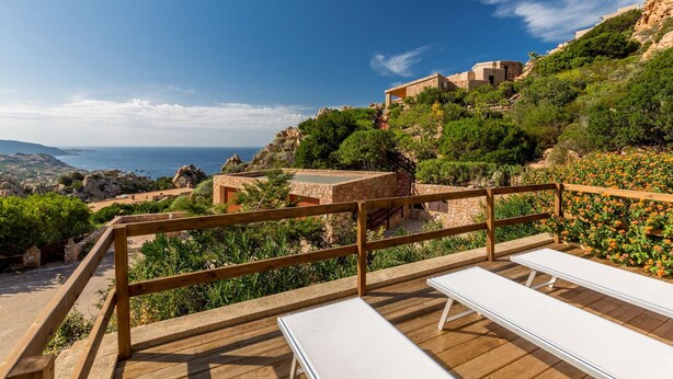 A wooden deck with white lounge chairs overlooking a coastal landscape with rocky terrain and a view of the sea. - Villa Violetta 1 Bianca (Trinità d'Agultu e Vignola)