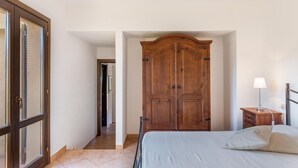 A bedroom with a large wooden wardrobe, a bed with white linens, and a bedside table with a lamp. - Villa Violetta 1 Bianca (Trinità d'Agultu e Vignola)