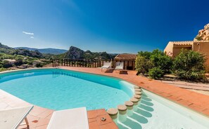 A swimming pool with a clear blue water, surrounded by a tiled deck and a stone wall. - Villa Violetta 1 Bianca (Trinità d'Agultu e Vignola)