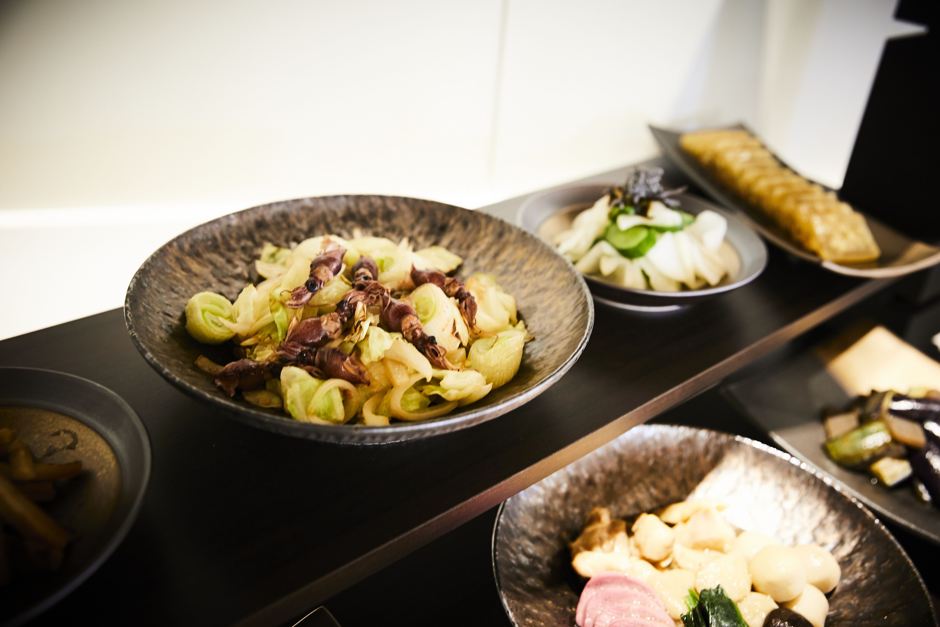 Uma mesa de jantar com diversos pratos, incluindo um prato de massa com carne e legumes, um prato de dumplings e um prato com berinjela.