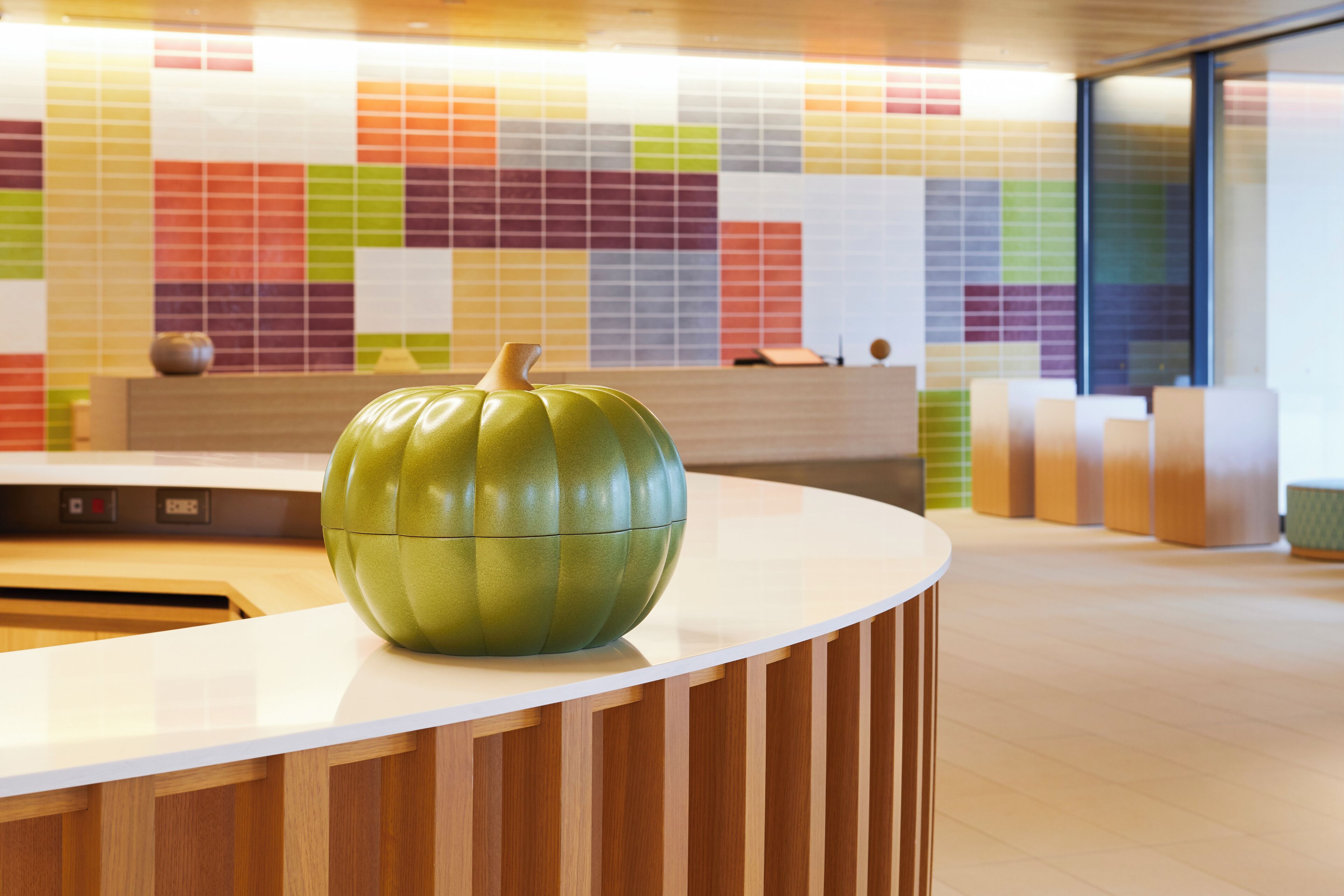 Un mostrador de recepción moderno con un objeto decorativo verde, una pared de azulejos coloridos y un suelo de madera.