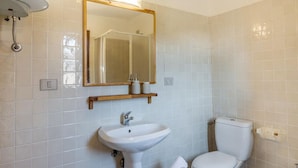 A bathroom with white tiled walls, a white sink, a toilet, and a mirror with a wooden frame.
