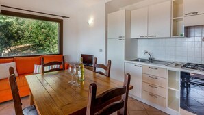 A modern kitchen with white cabinets, a dining table with chairs, and a window overlooking greenery.