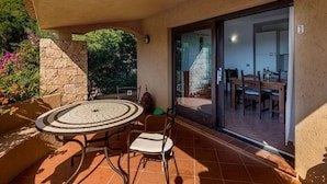 A patio with a round table and chairs, a stone wall, and a view of the interior through glass doors.