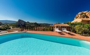 A swimming pool with two lounge chairs and a pergola, surrounded by a stone wall and a view of the mountains. - Villa Violetta 3 Verde (Trinità d'Agultu e Vignola)