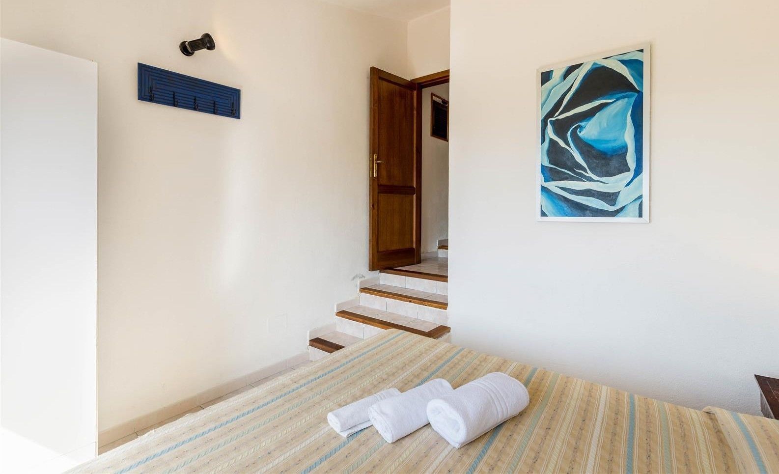 A hotel room with a bed, a striped rug, a painting, a wooden door, and a staircase.