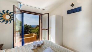 A bedroom with a bed, a view of the sea, and a balcony with a wooden bench. - Villetta Ginepro Rosso (Trinità d'Agultu e Vignola)