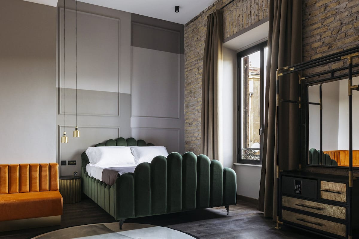 A modern bedroom with a green upholstered bed, a wooden nightstand, a sofa, and a large mirror.