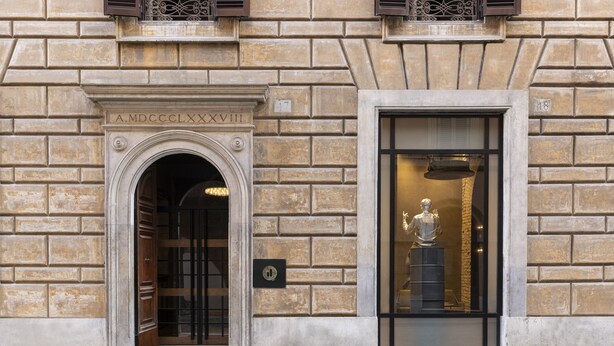 A building facade with a stone wall, a door with a sign, and a window with a statue. - Hotel Chapter Roma (Rome)