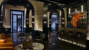 A modern bar area with a stone wall backdrop, bar stools, and a seating area with a round table and chairs. - Hotel Chapter Roma (Rome)