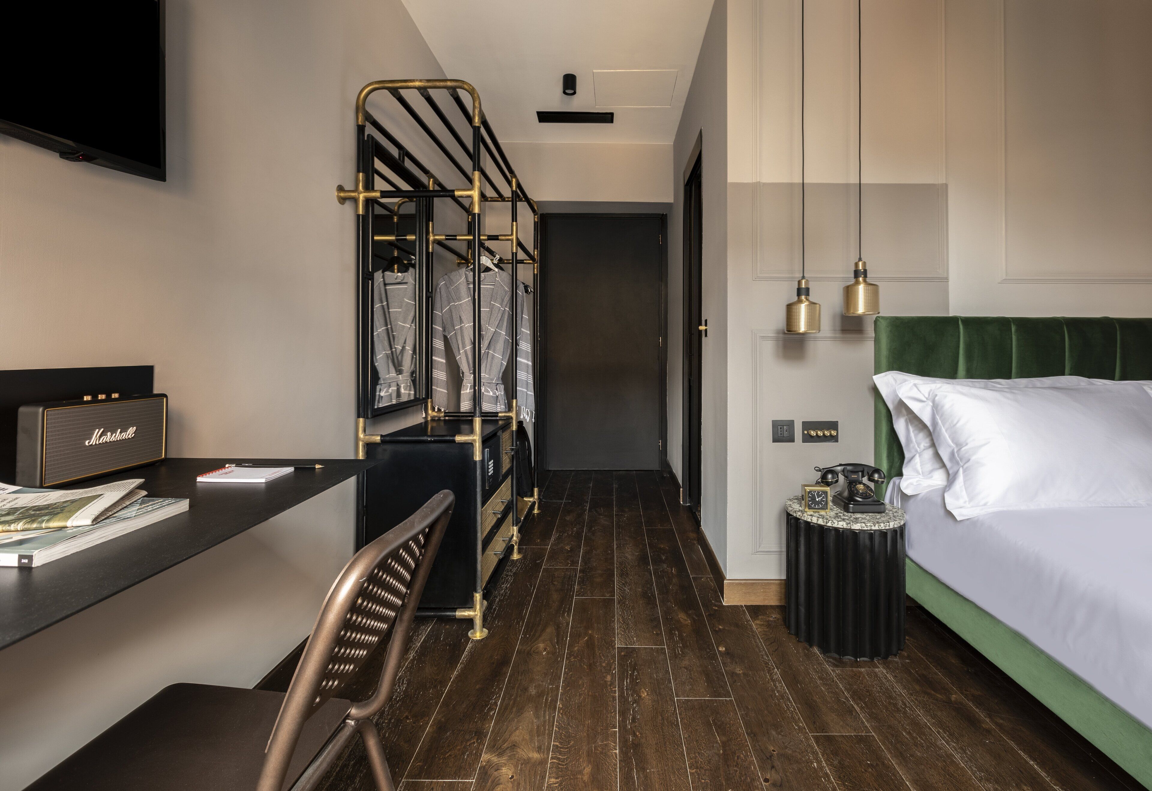 A hotel room with a desk, chair, bed, and a small table with a telephone.