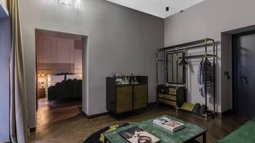 Ett modernt hotellrum med en minimalistisk design, inrett med en grön soffa, ett litet bord med tidningar, en garderob med spegel och en bardisk med flaskor.