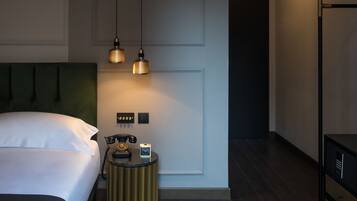 Una camera d'albergo moderna con un letto, un comodino e un tavolino rotondo con telefono e sveglia.