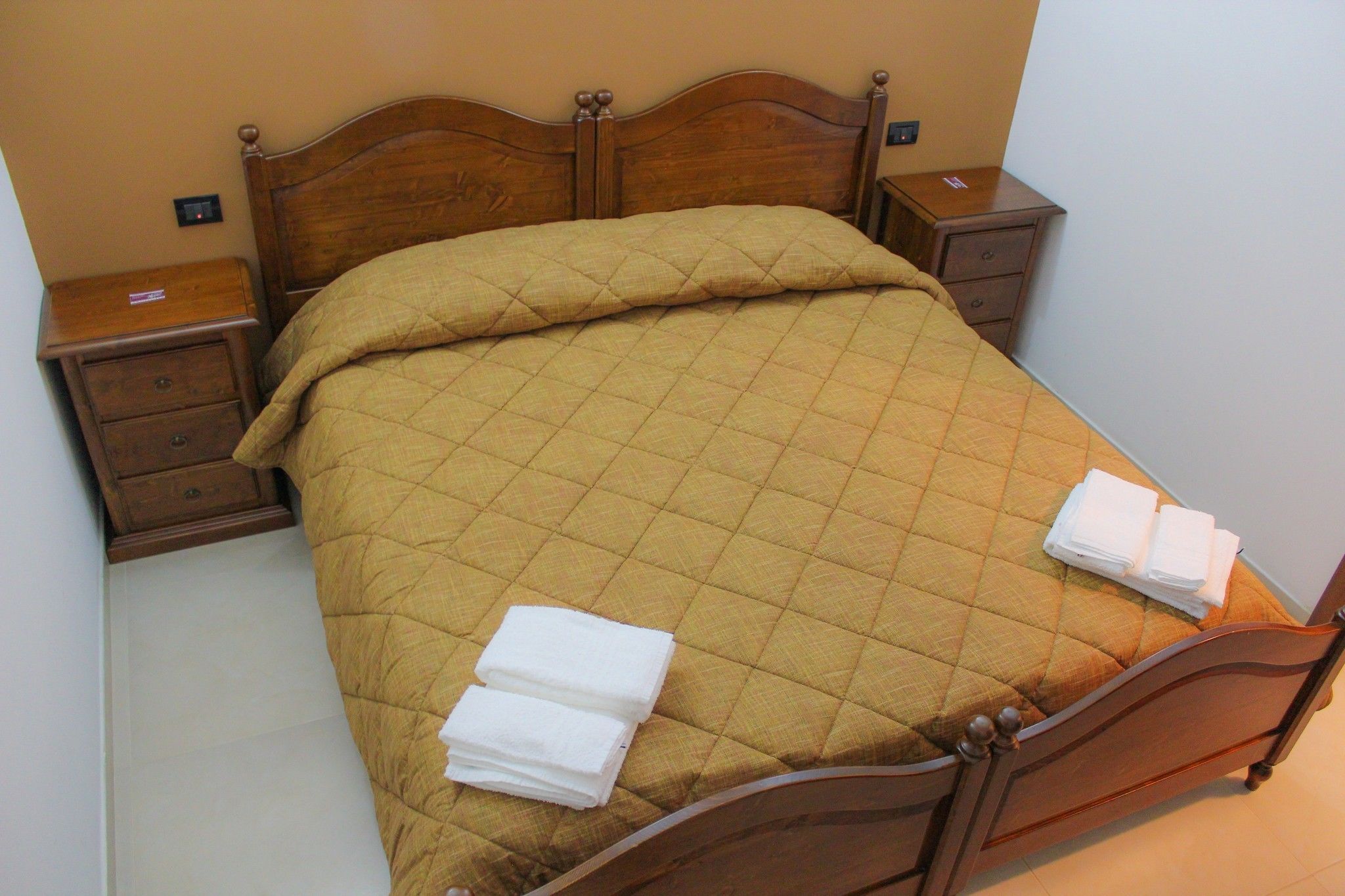 Una cama bien hecha con una colcha acolchada y dos toallas blancas dobladas al pie.
