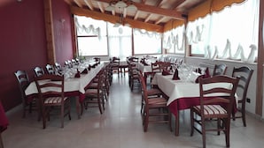 A long dining table set for a meal with chairs on both sides, wooden chairs with red cushions, and a tiled floor. - Agriturismo Rifugio di Dedalo (Sant'Angelo Muxaro)