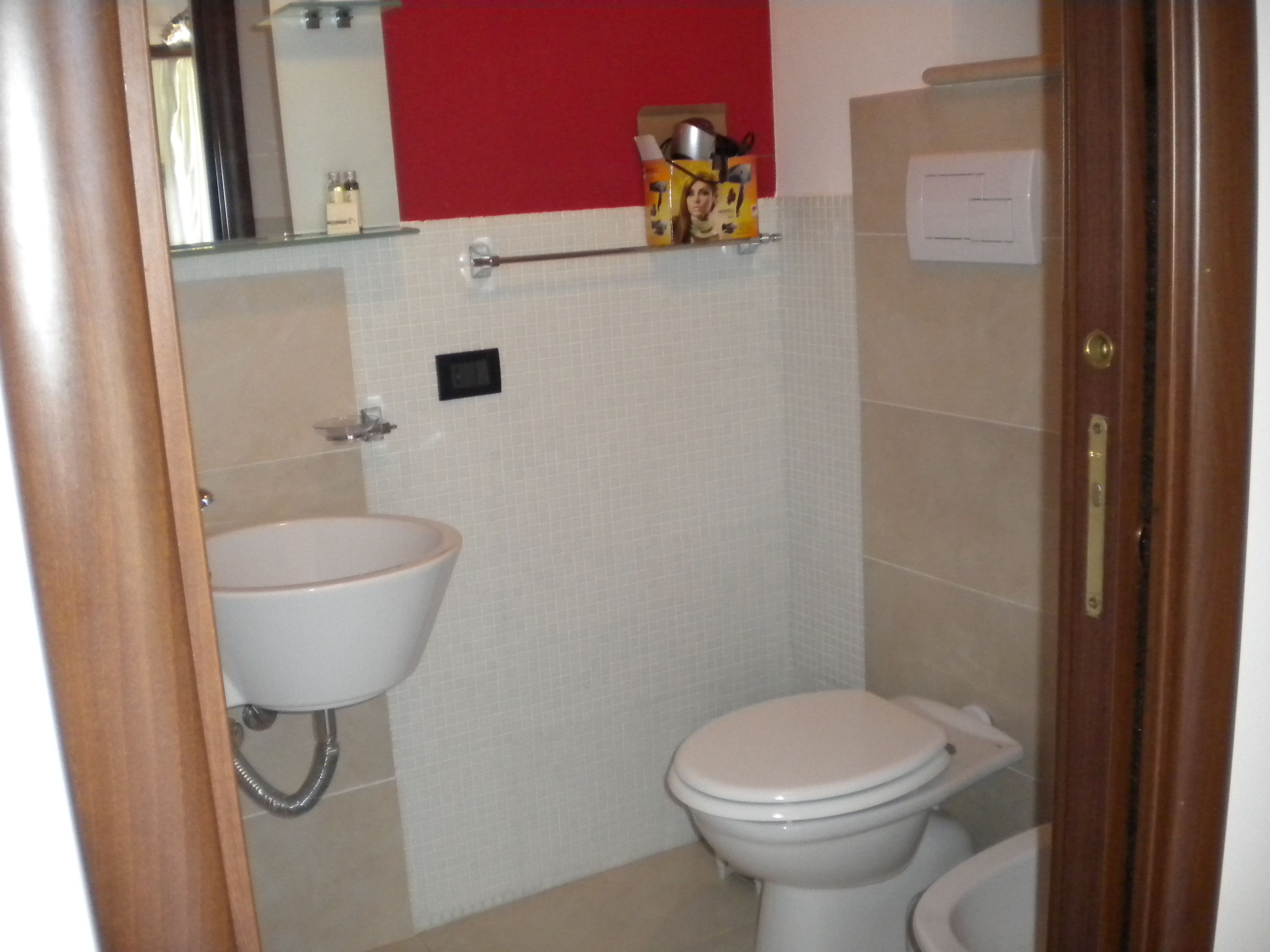 A bathroom with a white sink, a toilet, and a red accent wall.