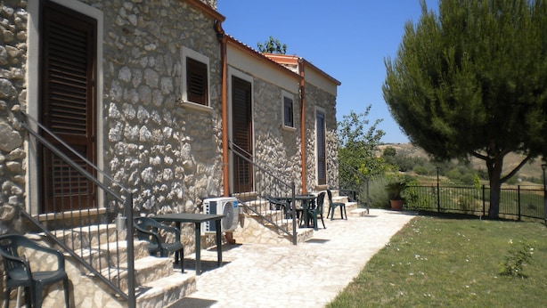 A stone building with a tiled roof, outdoor seating, and a large tree. - Agriturismo Rifugio di Dedalo (Sant'Angelo Muxaro)