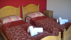 Two wooden beds with red and floral bedding, a small wooden nightstand, and a red wall. - Agriturismo Rifugio di Dedalo (Sant'Angelo Muxaro)