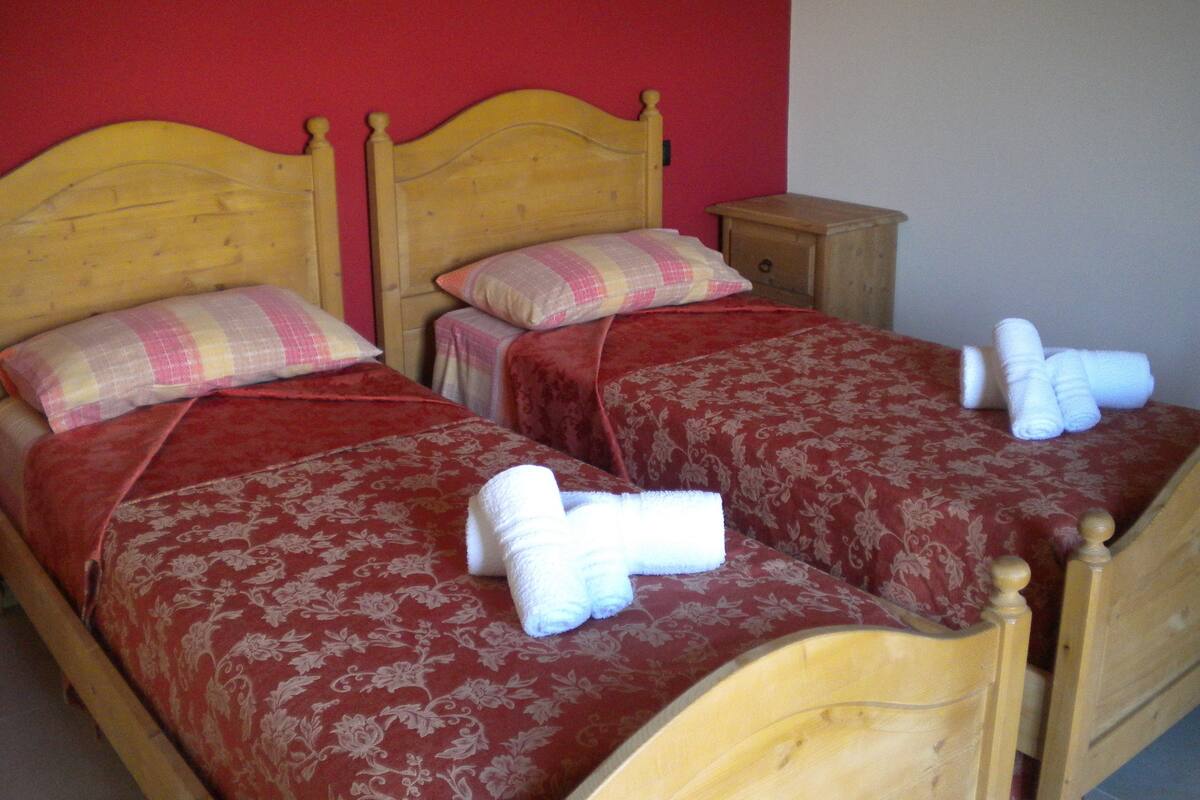 Two wooden beds with red and floral bedding, a small wooden nightstand, and a red wall.