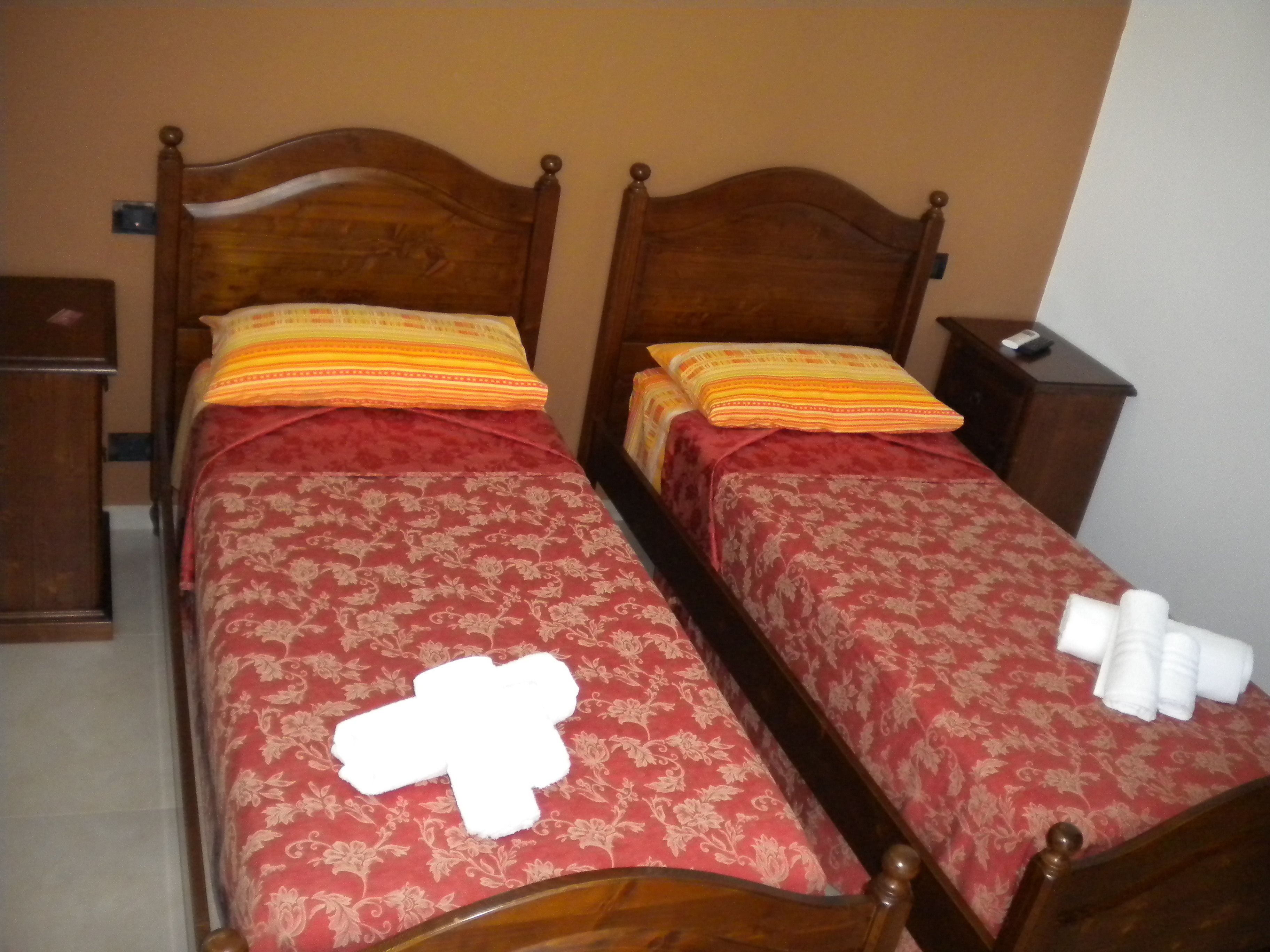 Two wooden beds with red floral bedspreads, pillows, and towels.