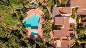 An aerial view of a resort with a large swimming pool, multiple villas, and lush greenery.