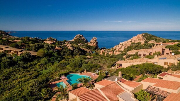 A coastal resort with a swimming pool, terraced houses, and rocky cliffs.