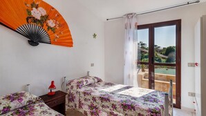 A bedroom with two beds, a red lamp, a fan, and a balcony with a view.