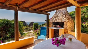 A patio with a stone oven, a table with a vase of flowers, and a view of the sea.