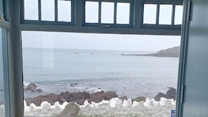 A small seating area with a view of the ocean through a window with multiple panes. - The Paris Hotel (Helston)