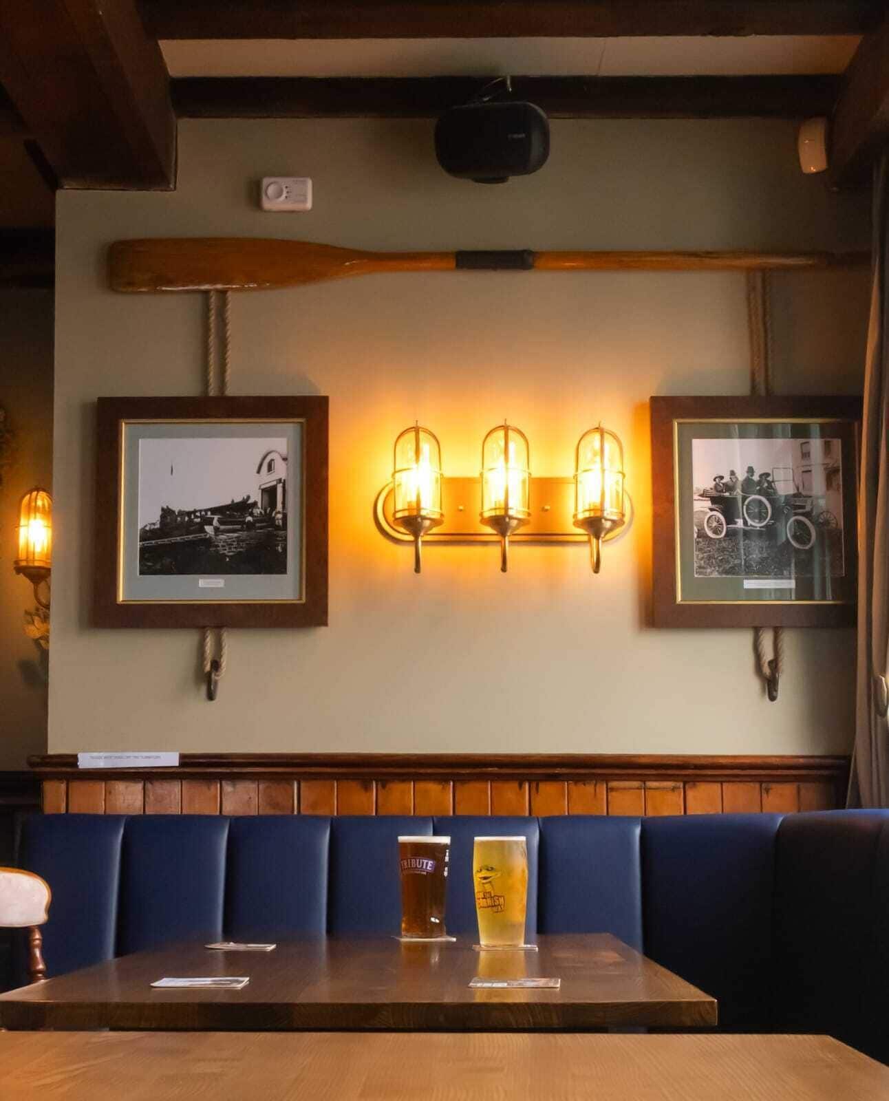 Interior de restaurante con bancos de madera, una mesa con bebidas e iluminación fijada a la pared.