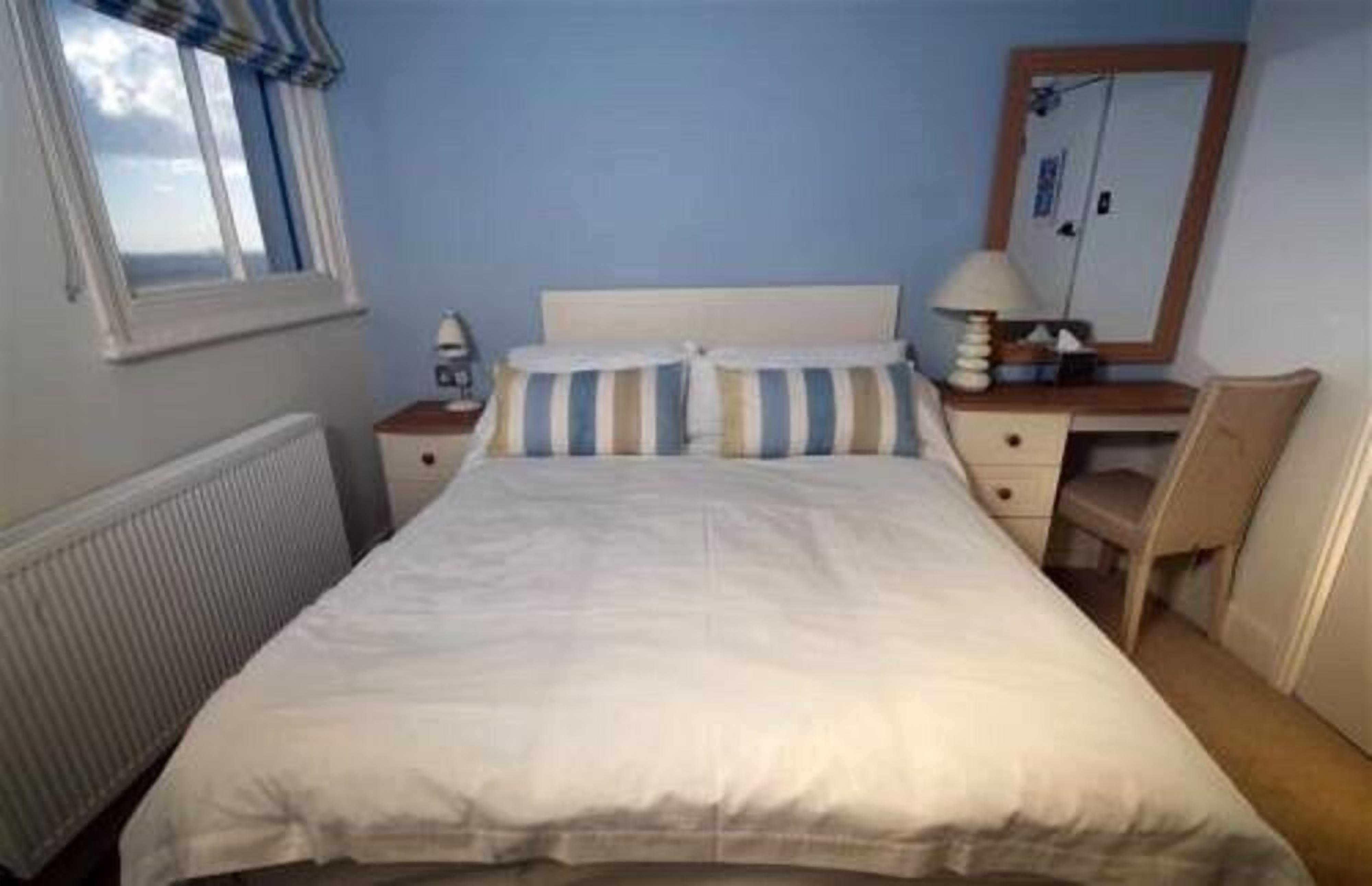 A bedroom with a bed, a nightstand, a lamp, a chair, and a window.
